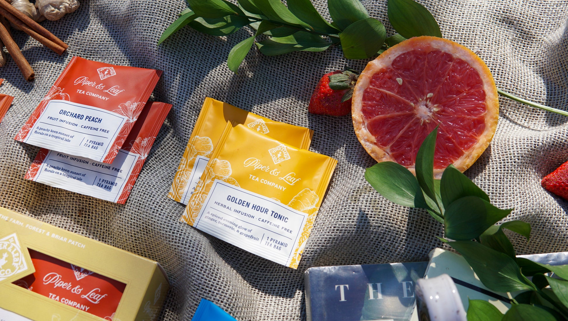 The Piper & Leaf Tea Co. Caffeine Free Sampler—Box of 16 tea bags—features Orchard Peach and Golden Hour Tonic flavors, displayed on fabric with fruit and leaves, perfect for your next herbal infusion or tea tasting flight.