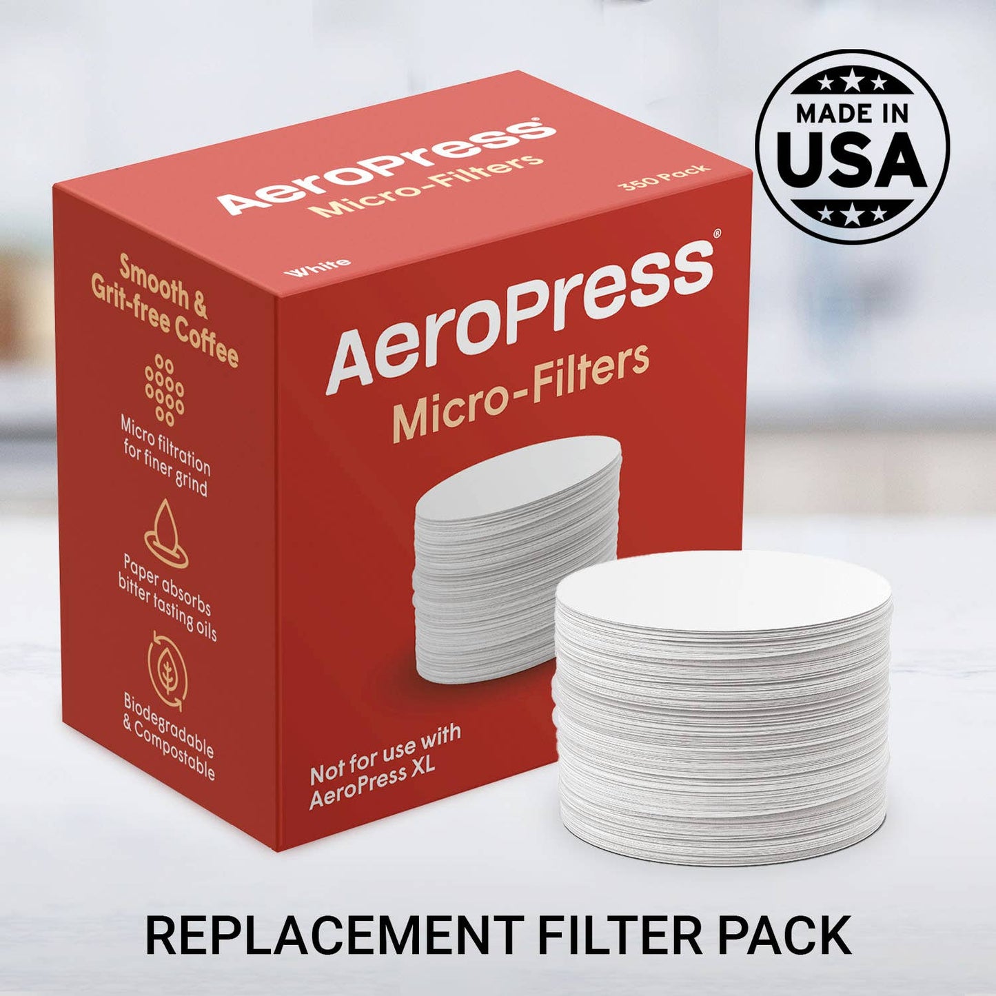 A box of AeroPress Paper Micro-Filters by AeroPress sits beside a stack of white round filters, with a "Made in USA" badge in the background. Text reads: REPLACEMENT FILTER PACK.