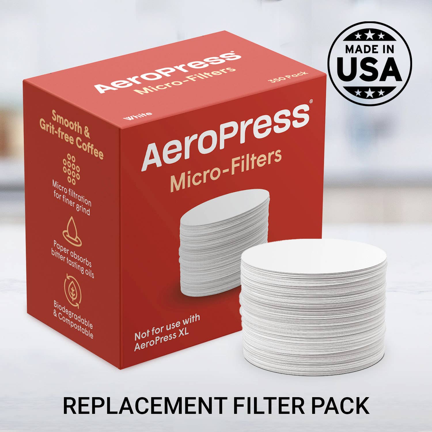 A box of AeroPress Paper Micro-Filters by AeroPress sits beside a stack of white round filters, with a "Made in USA" badge in the background. Text reads: REPLACEMENT FILTER PACK.