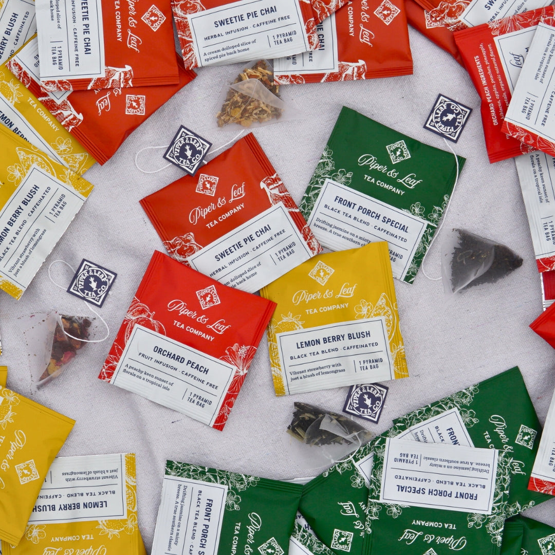 Piper & Leaf Tea Co.'s Bestselling Blends - 50ct Tea Bags, featuring caffeine-free herbal infusions like Sweetie Pie Chai and Orchard Peach, along with black tea blends like Front Porch Special and Lemon Berry Blush, are scattered on a surface.