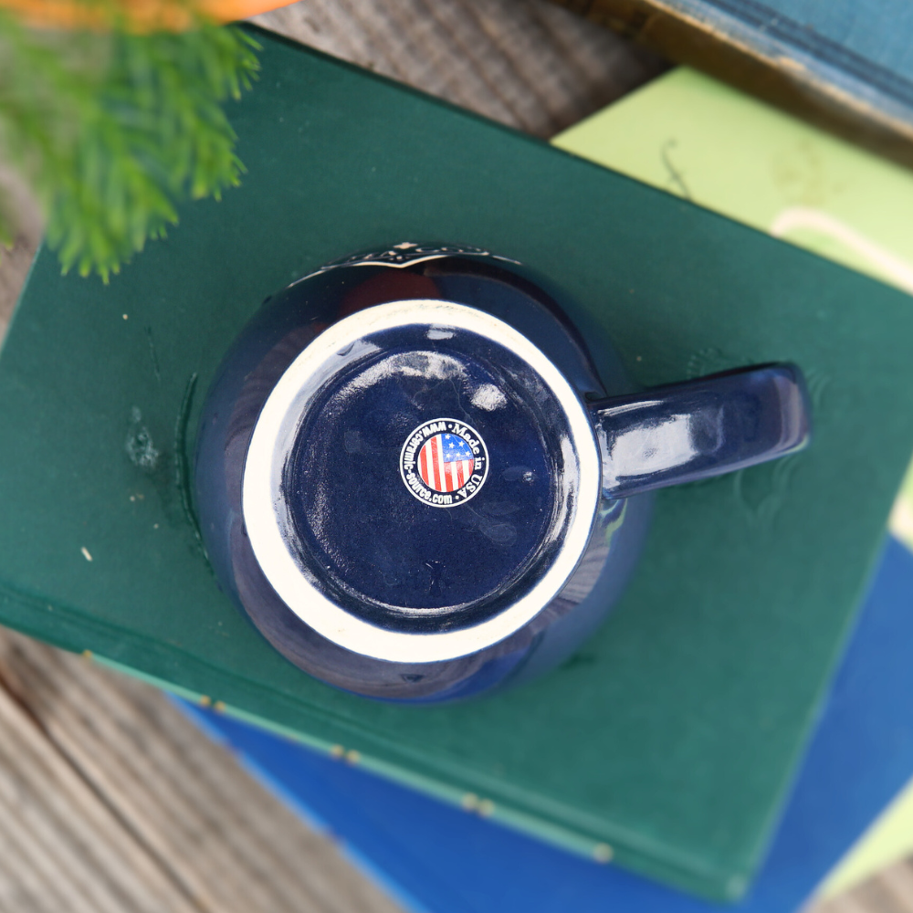 Overhead view of a Piper & Leaf Tea Co. 12oz Sand Carved Logo Mug in gloss blue, placed on a stack of books.