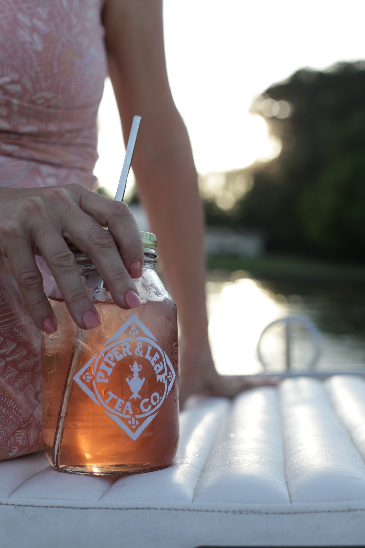 A woman sitting on a boat holding a Signature Mason Drinking Jar - Quart Size of Piper & Leaf Tea Co.iced tea.
