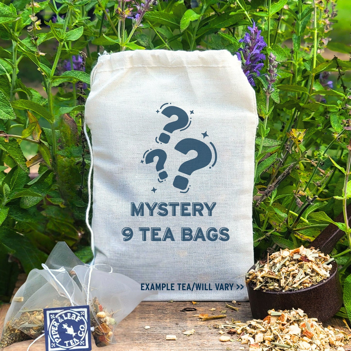A muslin bag labeled "Mystery 9ct Tea Bags in Muslin" by Piper and Leaf Tea Co. rests on wood with a tea infuser, loose tea blends, and greenery in the background.