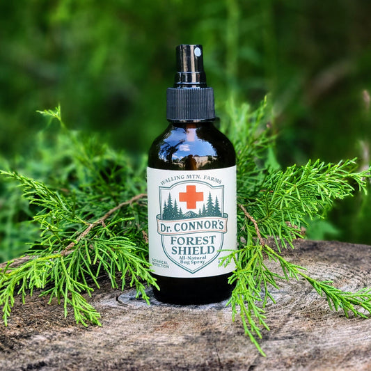 A bottle of Walling Mountain Farms' Dr. Connor's Forest Shield All-Natural Bug Spray, a DEET-free insect repellent, sits on a tree stump with green foliage in the background.