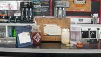A Piper and Leaf Tea Co. Root Beer Tea Brew Kit, with concentrated tea, brewed root beer, sugar, and a brewing container, is displayed on a café counter.