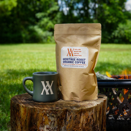 The Walling Mtn. Coffee + Mug Bundle from Walling Mtn. Coffee rests on a tree stump outdoors near a fire pit.