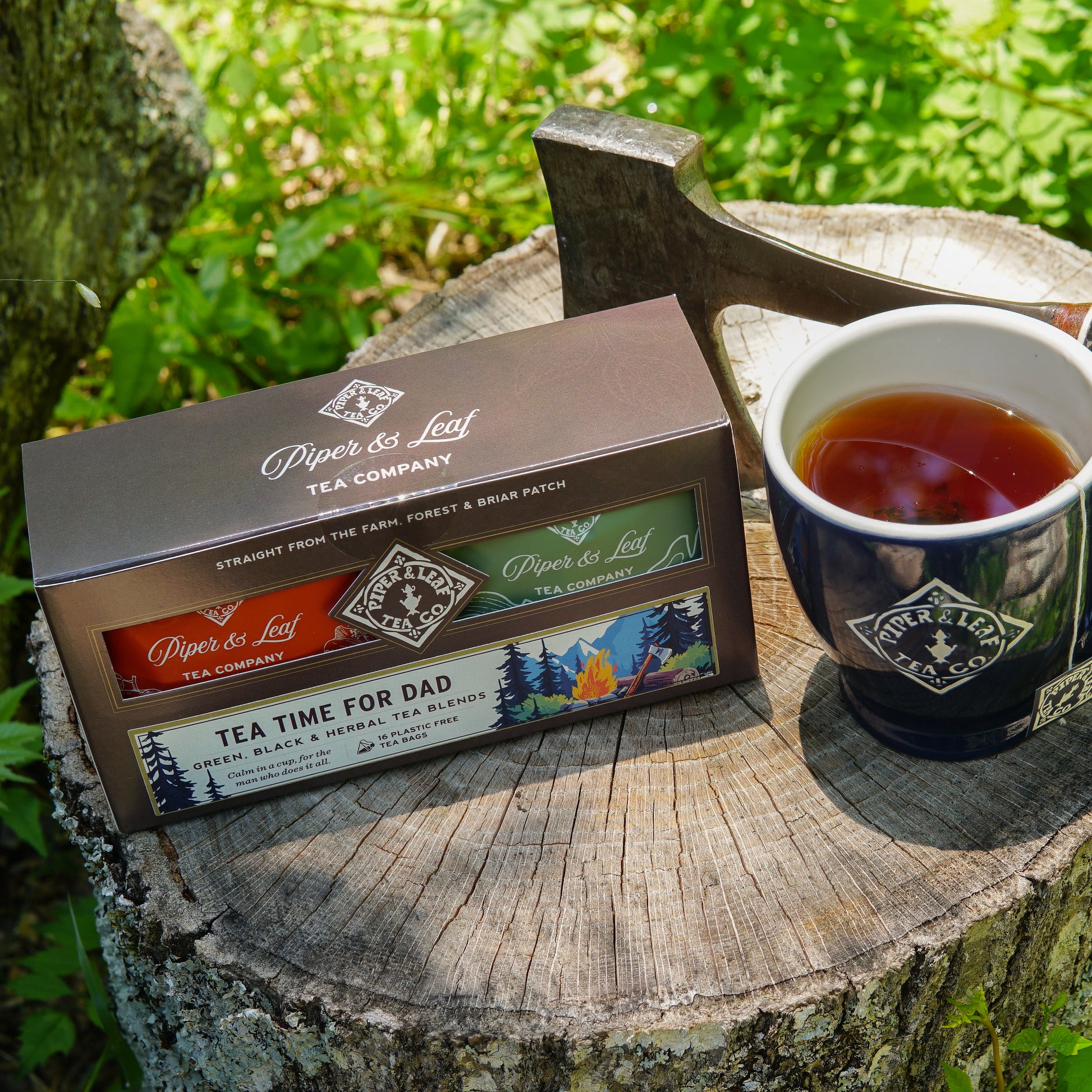The "Tea Time For Dad- Box of 16 Individually Wrapped Tea Bags" from Piper & Leaf Tea Co. is displayed beside a mug, axe, and greenery—an ideal Father’s Day gift for tea-loving dads.