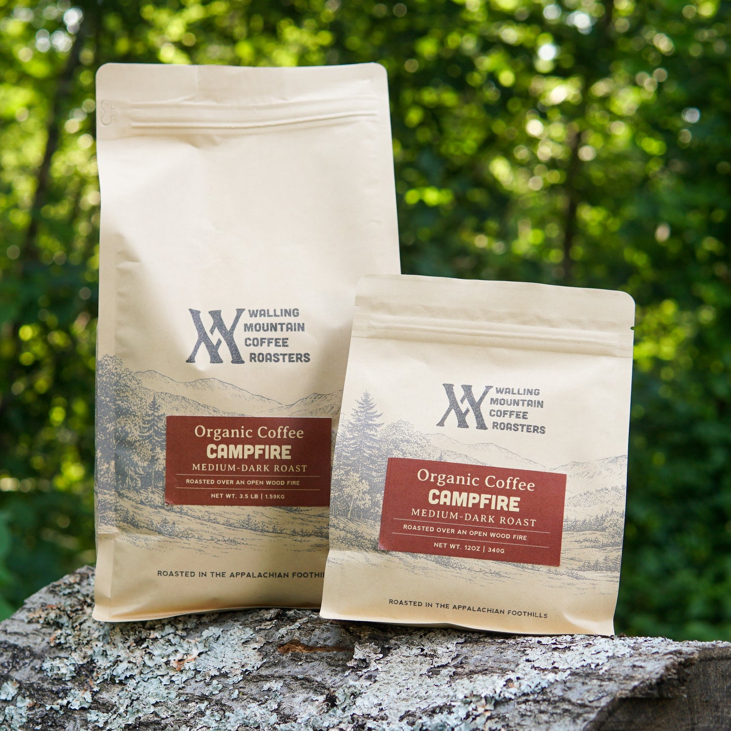 Two 3.5lb bags of Walling Mtn. Coffee's Campfire Roast, expertly roasted over an open flame, rest on a rock with trees and greenery in the background. Experience the rich flavor of this small-batch coffee in every cup.