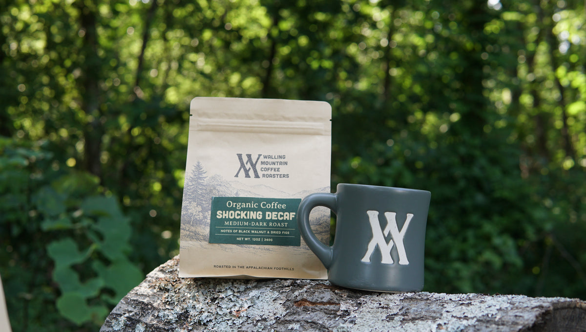 A 12oz Bag of Decaf Coffee — Walling Mtn. and a matching mug rest on a tree trunk, with the forest in the background.