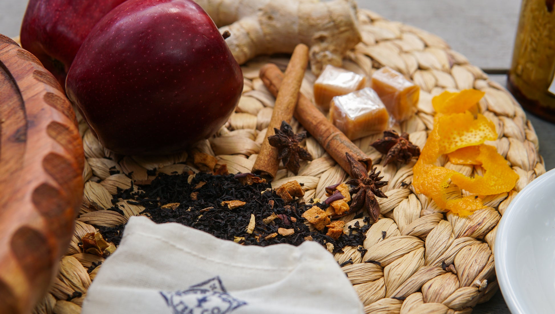 A close-up of Piper & Leaf Tea Co.'s Caramel Apple Pie Muslin Bag of Loose Leaf Tea—featuring visible ingredients like red apple, ginger, cinnamon sticks, star anise, orange peel, caramel candies, and tea leaves spilling from the cloth bag.
