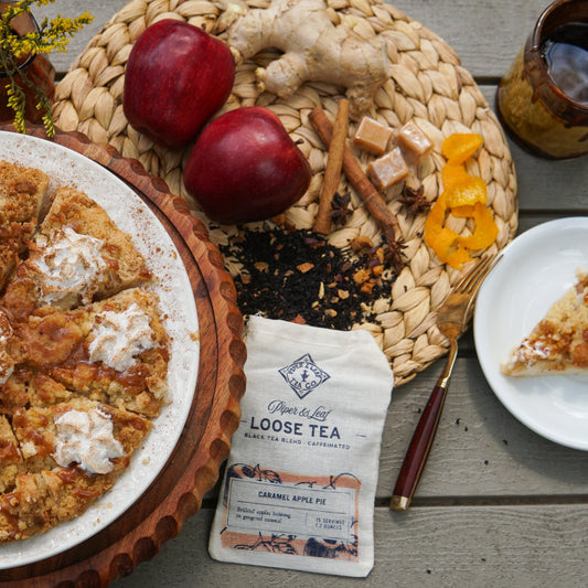 A sliced apple pie with whipped topping, apples, ginger, caramel, orange peel, and a served slice—perfectly paired with Piper & Leaf Tea Co.'s Caramel Apple Pie Muslin Bag of Loose Leaf Tea (15 servings).