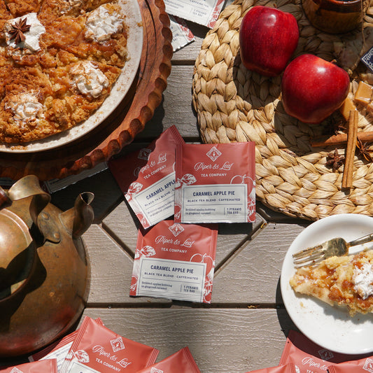 Piper & Leaf Tea Co.'s Caramel Apple Pie Case of Individually Wrapped Tea Bags (50ct) makes the perfect gift, featuring tea bags with a slice of pie, red apples, and a teapot arranged elegantly on a wooden table.