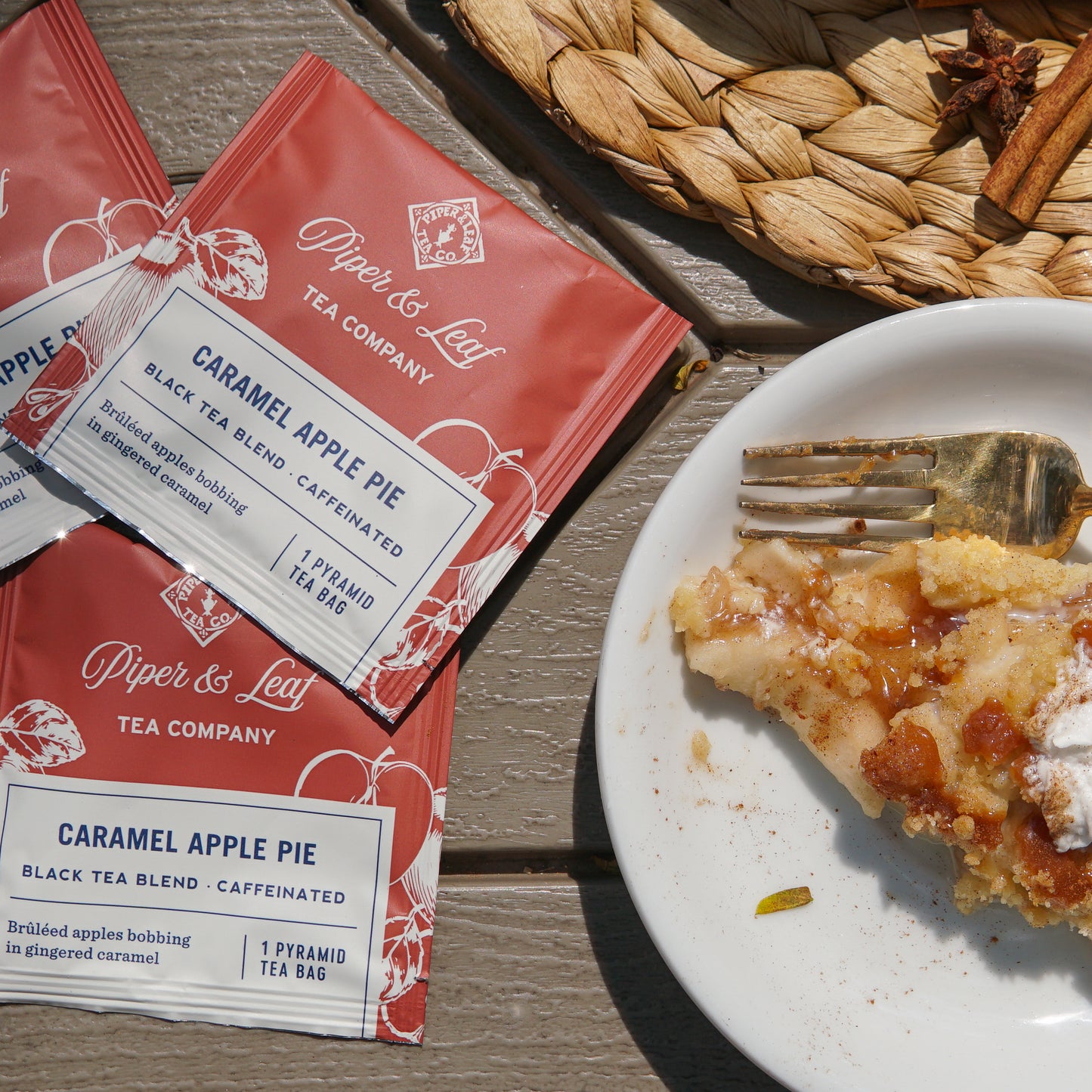 A case of 50 Piper & Leaf Tea Co. Caramel Apple Pie individually wrapped tea bags sits beside a partially eaten slice of apple pie on a white plate with a fork, all arranged on a woven mat.