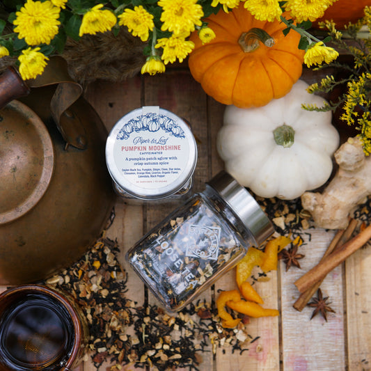 Assorted autumn items on wood, featuring Piper & Leaf Tea Co.’s Pumpkin Moonshine Glass Jar of Loose Leaf Tea (30 servings), pumpkins, yellow flowers, and a copper kettle—perfect for savoring cozy fall tea moments.