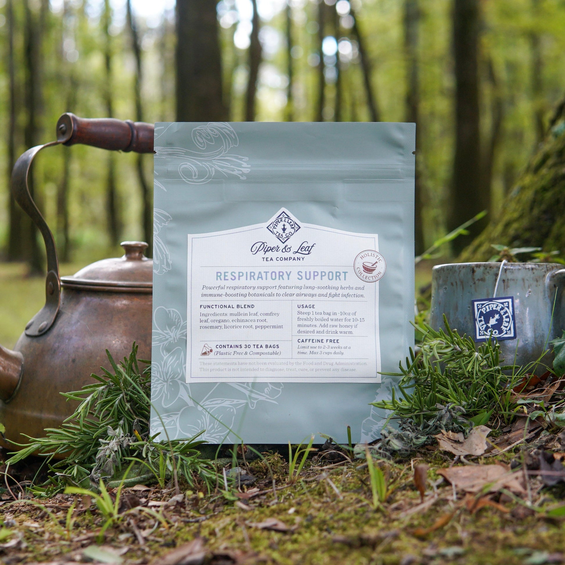 A bag of Piper and Leaf Tea Co. Respiratory Support sits on grass beside a teapot and mug, surrounded by lush greenery—an ideal herbal tea for supporting respiratory health and easy breathing.