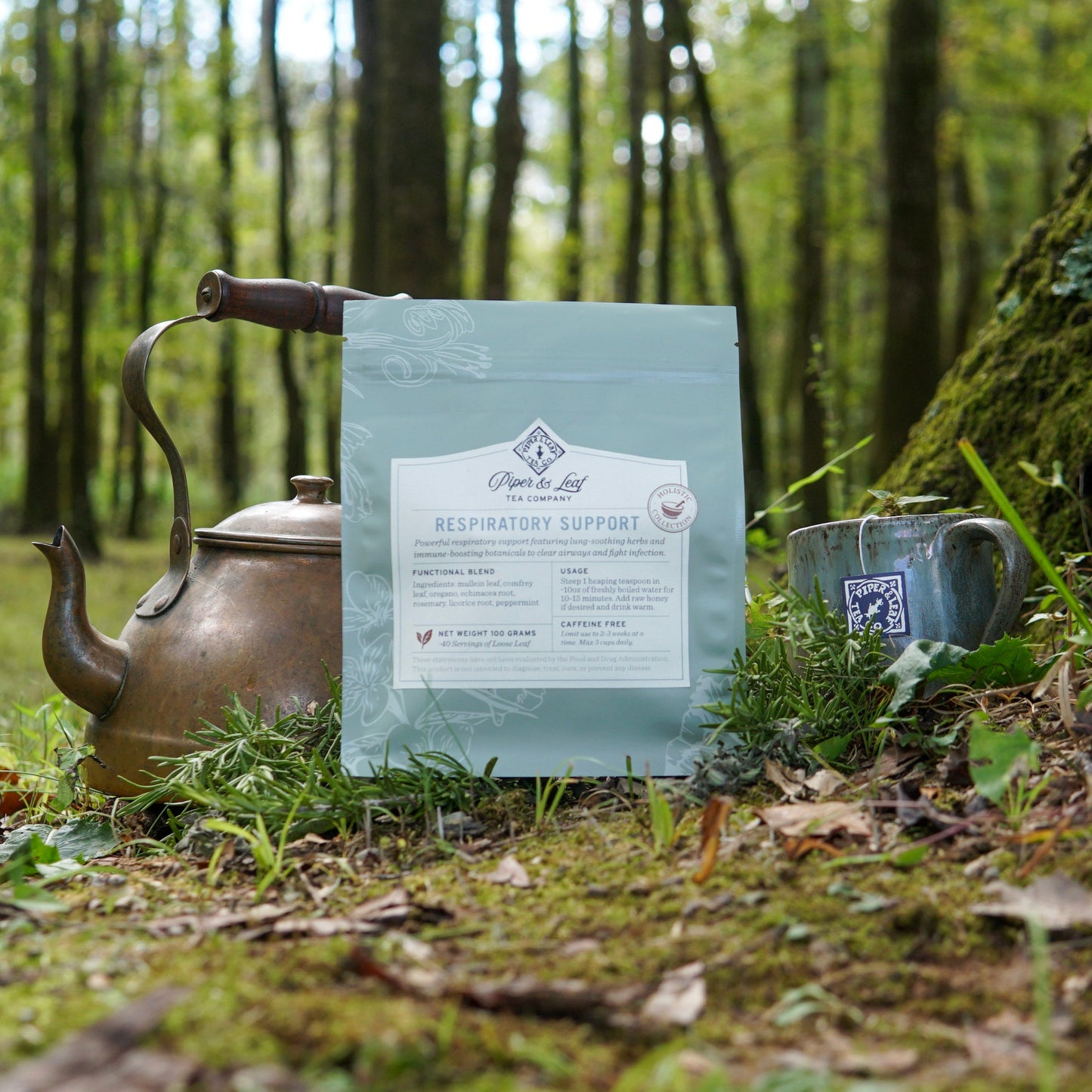 A "Respiratory Support" tea blend from Piper and Leaf Tea Co. rests on mossy ground beside a teapot and cup in the forest—inviting you to savor herbal support for easy breathing, surrounded by nature.