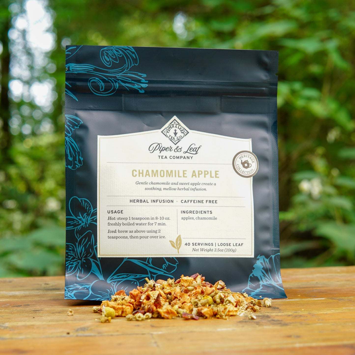 A bag of Piper and Leaf Tea Co.’s Chamomile Apple 40 Serving Loose Leaf Tea rests on a wooden surface outdoors, with dried tea leaves scattered in front, highlighting this soothing caffeine-free herbal infusion.