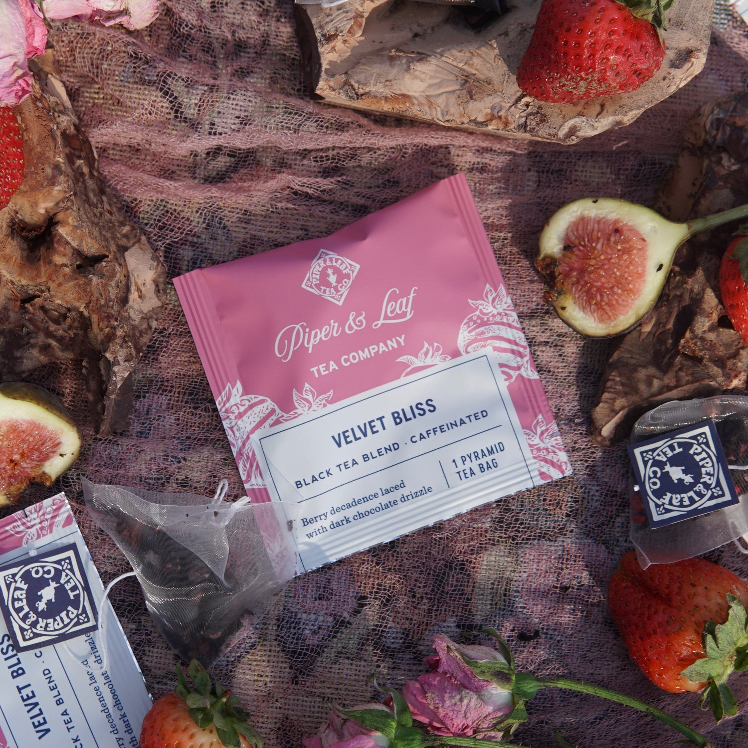 A Piper & Leaf Tea Co. Velvet Bliss Case of Individually Wrapped Tea Bags (50ct) is displayed on fabric with strawberries, figs, and single-serve sachets—ideal for bulk orders or crafting distinctive tea gift baskets.