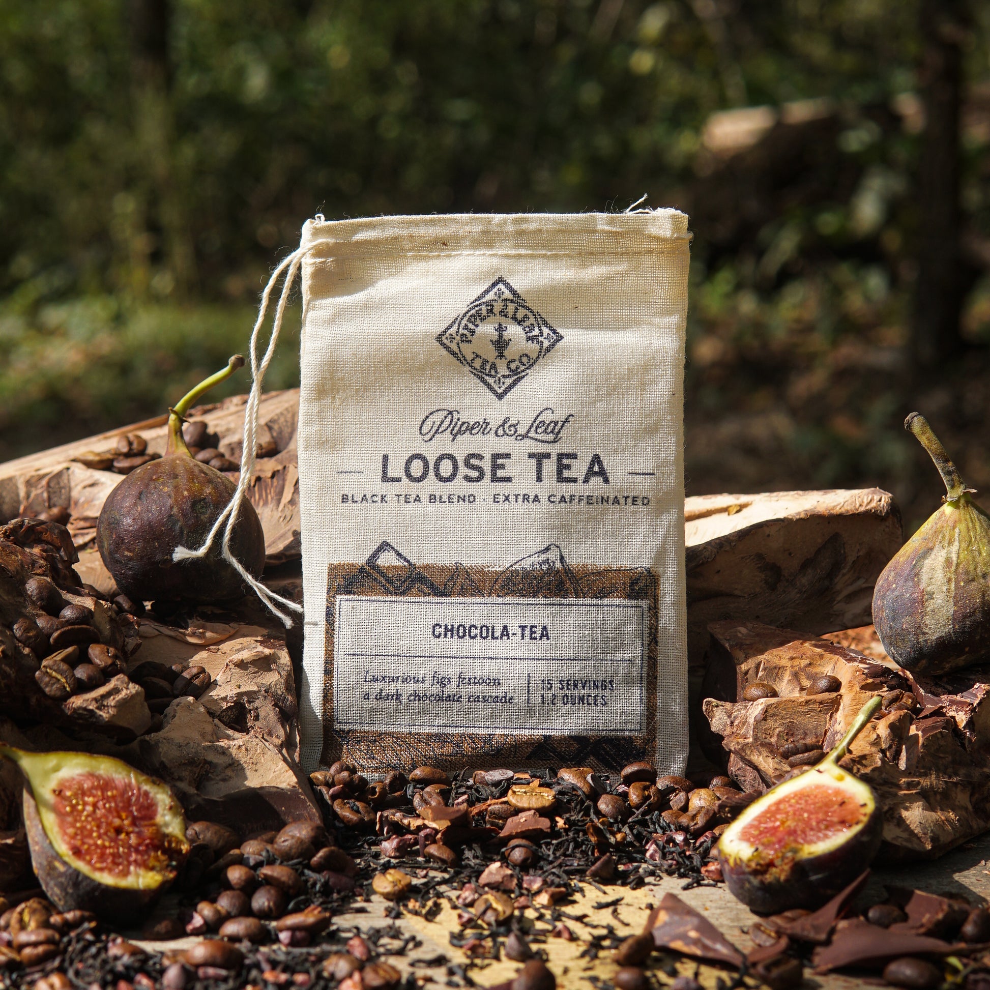 A Piper & Leaf Tea Co. Chocola-Tea Muslin Bag of Loose Leaf Tea (15 Servings) is displayed outdoors with figs, cocoa beans, and tea leaves, showcasing its rich chocolate fig and Ceylon black tea blend.