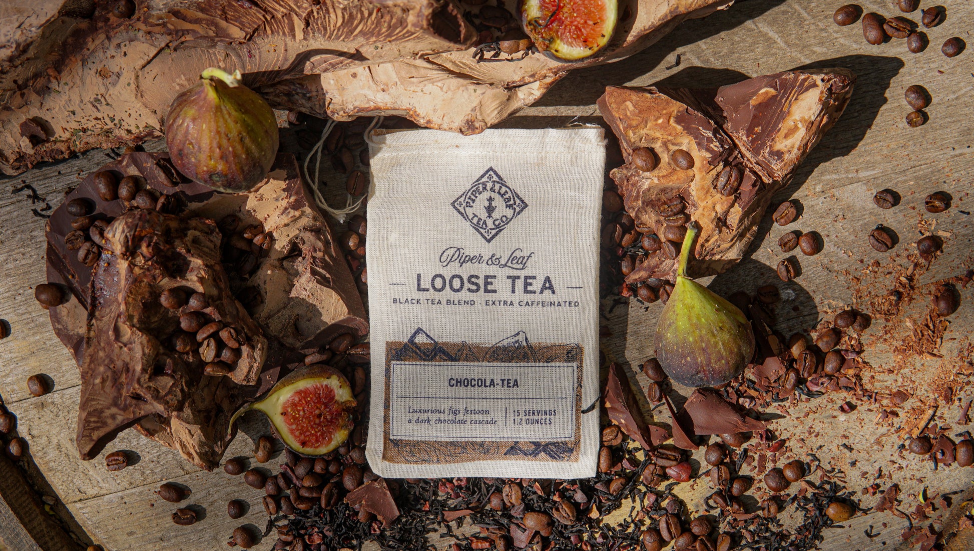 A Piper & Leaf Tea Co. Chocola-Tea Muslin Bag of Loose Leaf Tea (15 servings) sits on a wooden surface, surrounded by figs, chocolate pieces, coffee beans, and loose leaf tea, evoking the rich flavors of chocolate fig tea.