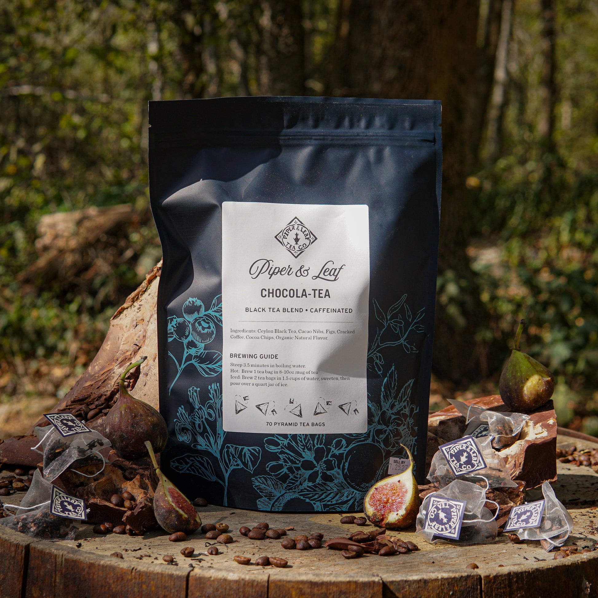 A bag of Piper & Leaf Tea Co. Chocola-Tea Bulk Sachets—70ct tea bags—is shown outdoors, surrounded by tea bags, cocoa beans, and fresh figs.