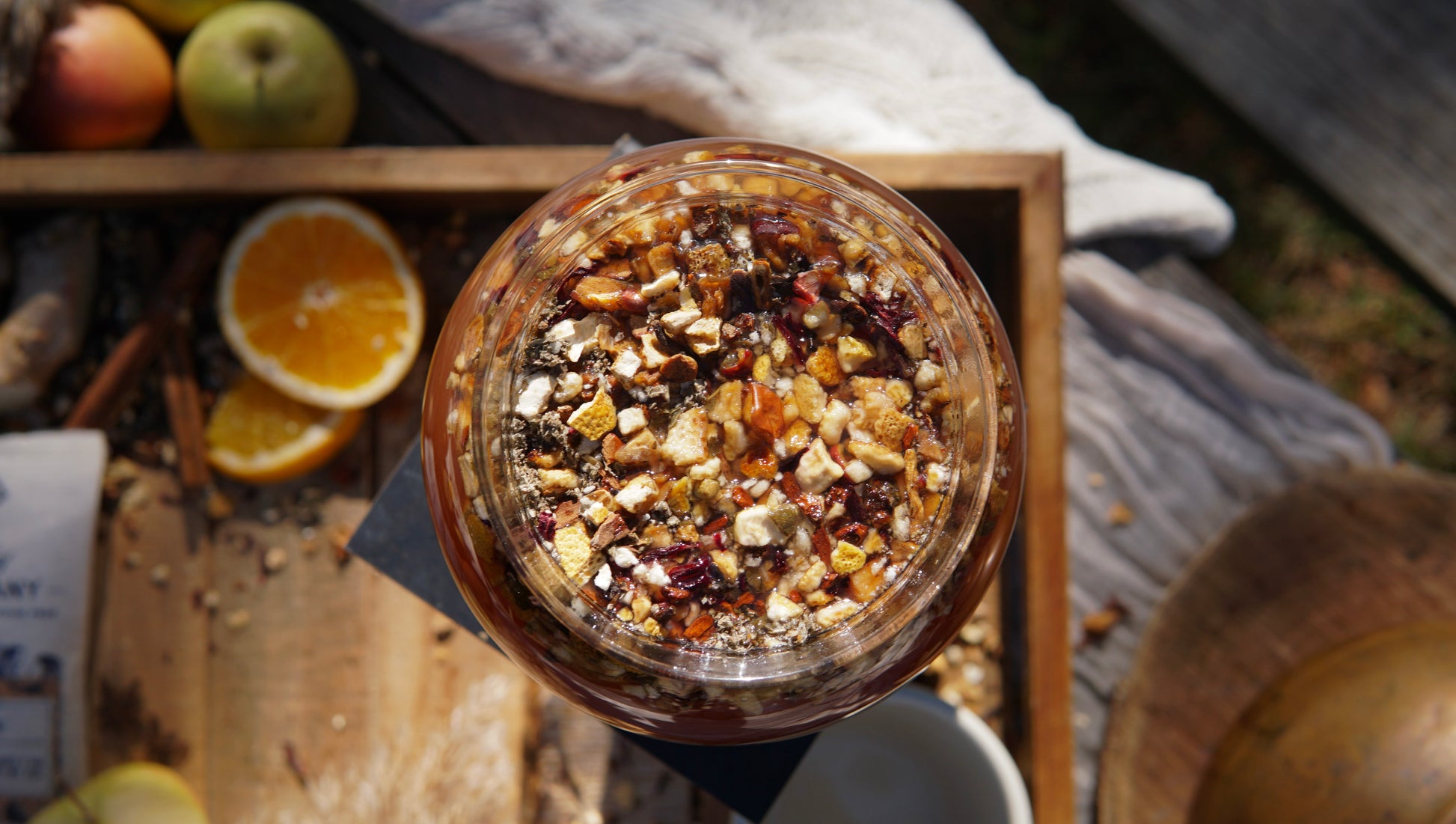 A top-down view of a glass jar filled with dried fruits and nuts beside sliced oranges and apples—an inviting spread to enjoy with Piper & Leaf Tea Co.'s Mulling Spice Mix, perfect for festive gatherings or sipping homemade spiced cider.