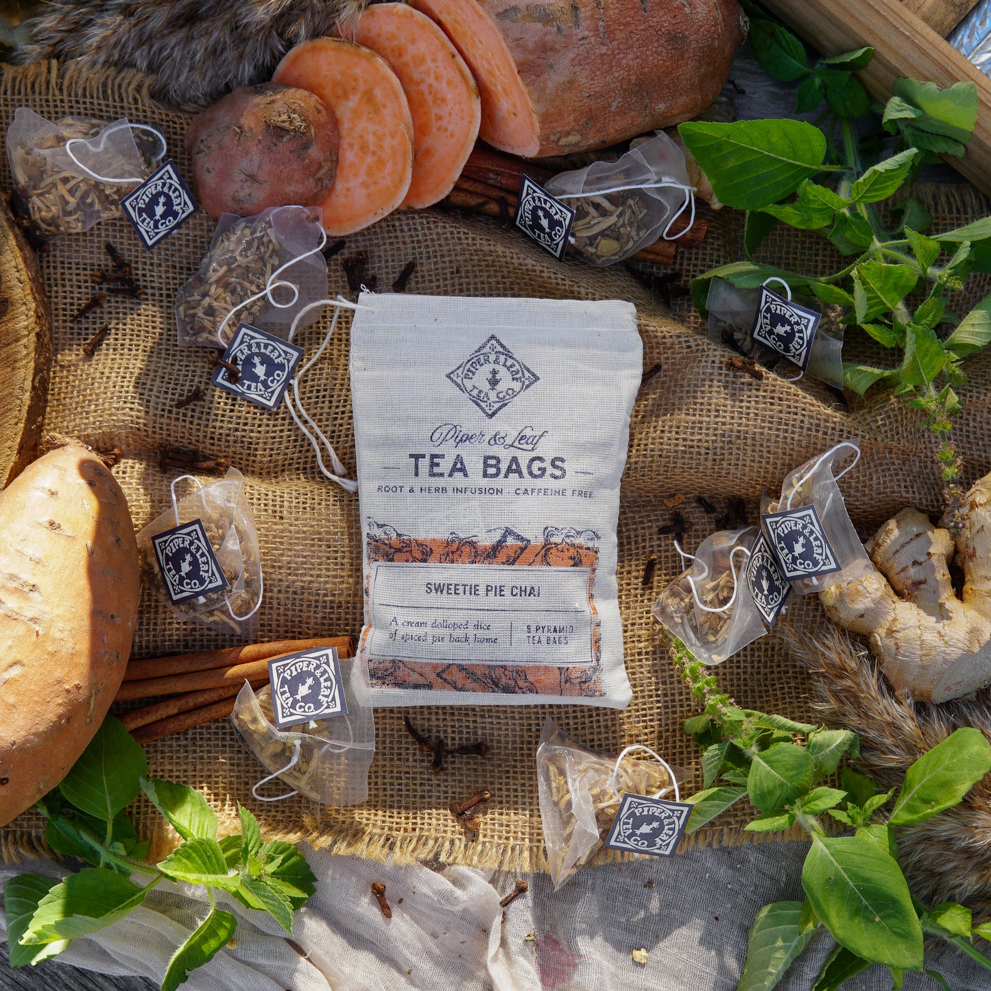 Piper & Leaf Tea Co. Sweetie Pie Chai 9ct Tea Bags in Muslin, caffeine free, displayed with spiced tea bags, candied sweet potato, bread, leafy herbs, and spices on burlap fabric.