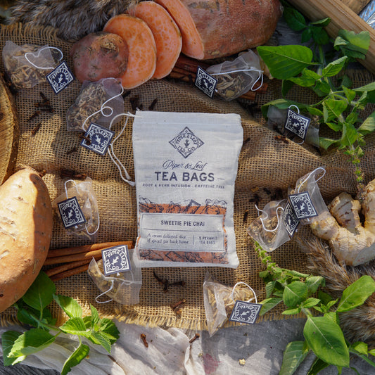 Piper & Leaf Tea Co. Sweetie Pie Chai 9ct Tea Bags in Muslin, caffeine free, displayed with spiced tea bags, candied sweet potato, bread, leafy herbs, and spices on burlap fabric.