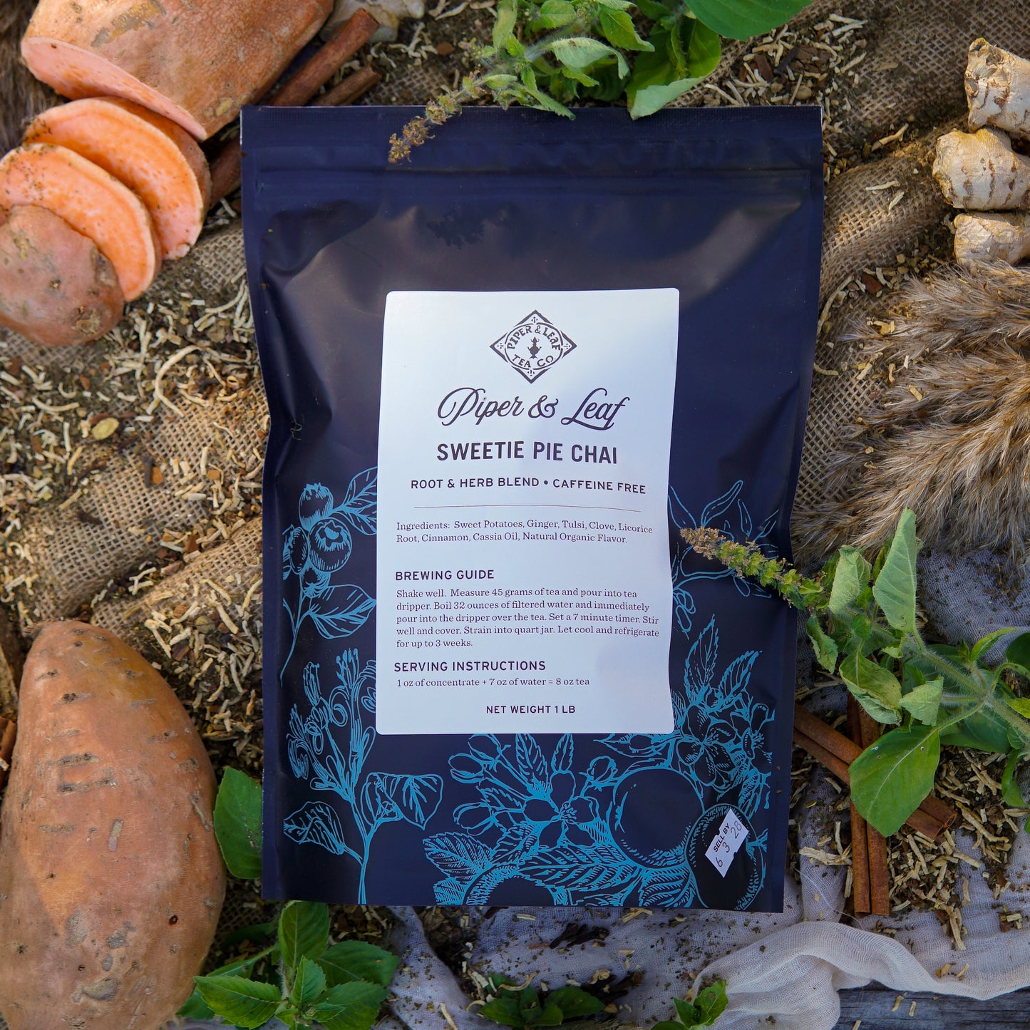 A Piper & Leaf Tea Co. Sweetie Pie Chai Pound Bag (190 servings) sits on the ground, surrounded by sweet potatoes, dried mushrooms, and green leaves.