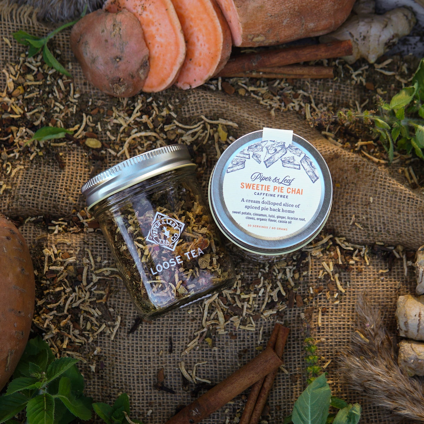 A Piper & Leaf Tea Co. Sweetie Pie Chai Glass Jar of Loose Leaf Tea (30 Servings) sits on burlap, surrounded by sweet potatoes, spices, and cinnamon—perfect for a flavorful, caffeine-free Sweet Potato Chai.