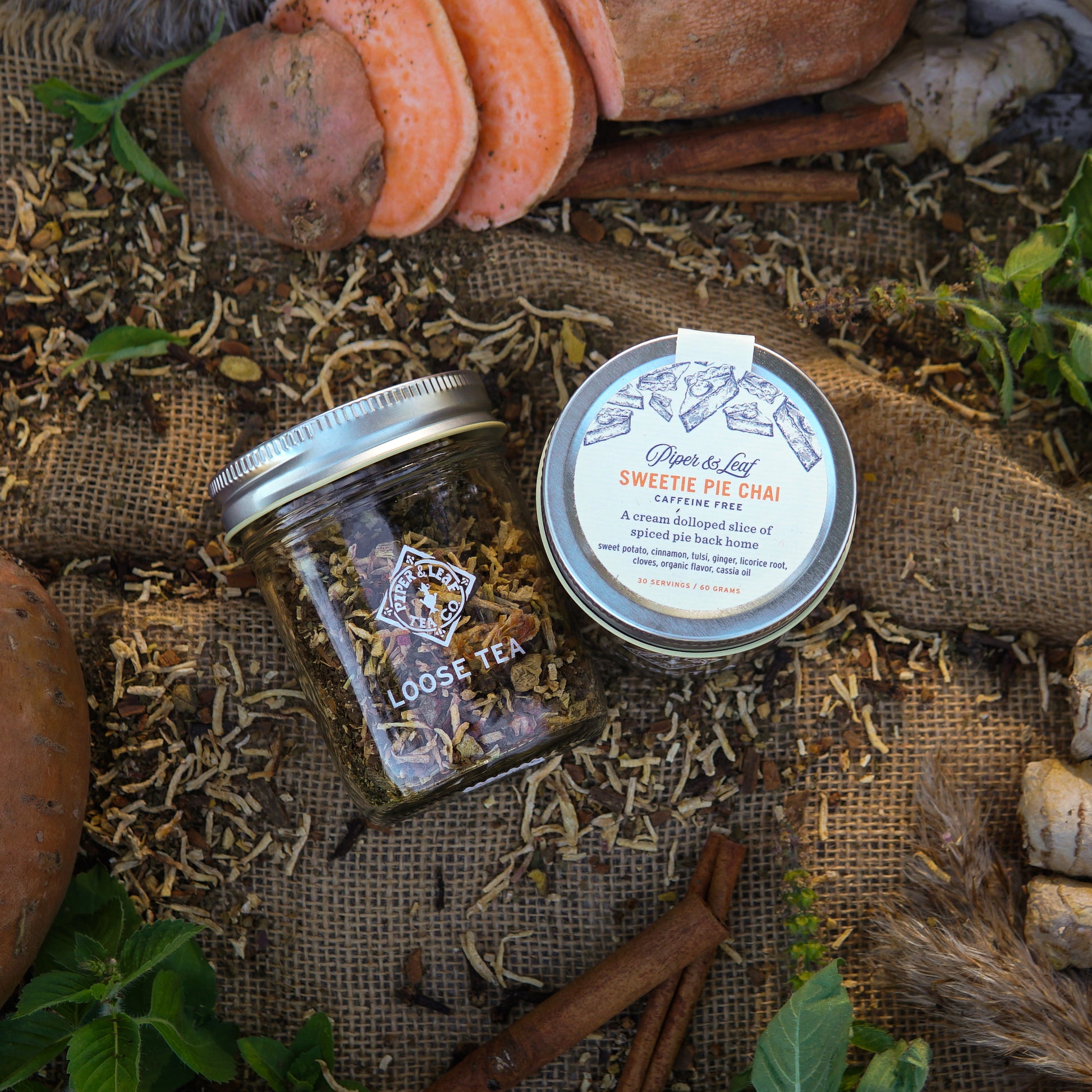 A Piper & Leaf Tea Co. Sweetie Pie Chai Glass Jar of Loose Leaf Tea (30 Servings) sits on burlap, surrounded by sweet potatoes, spices, and cinnamon—perfect for a flavorful, caffeine-free Sweet Potato Chai.