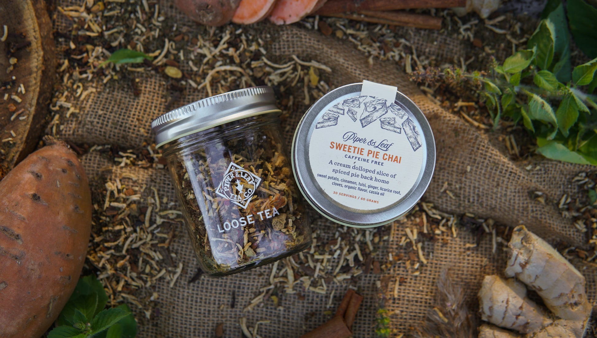 A Piper & Leaf Tea Co. Sweetie Pie Chai glass jar and tin rest on burlap with loose tea, sweet potatoes, and ginger, evoking the cozy, caffeine-free blend in this 30-serving loose leaf tea.