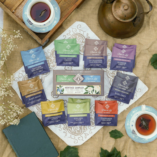 Heritage Sampler box on a lace and burlap backdrop surrounded by dried flowers, book, and tea