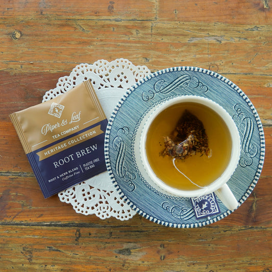 A Piper and Leaf Tea Co. “Root Brew” 50ct Individually Wrapped Tea Bag from the Heritage Collection rests on a wooden surface. The package is brown and navy, adorned with white and gold lettering.