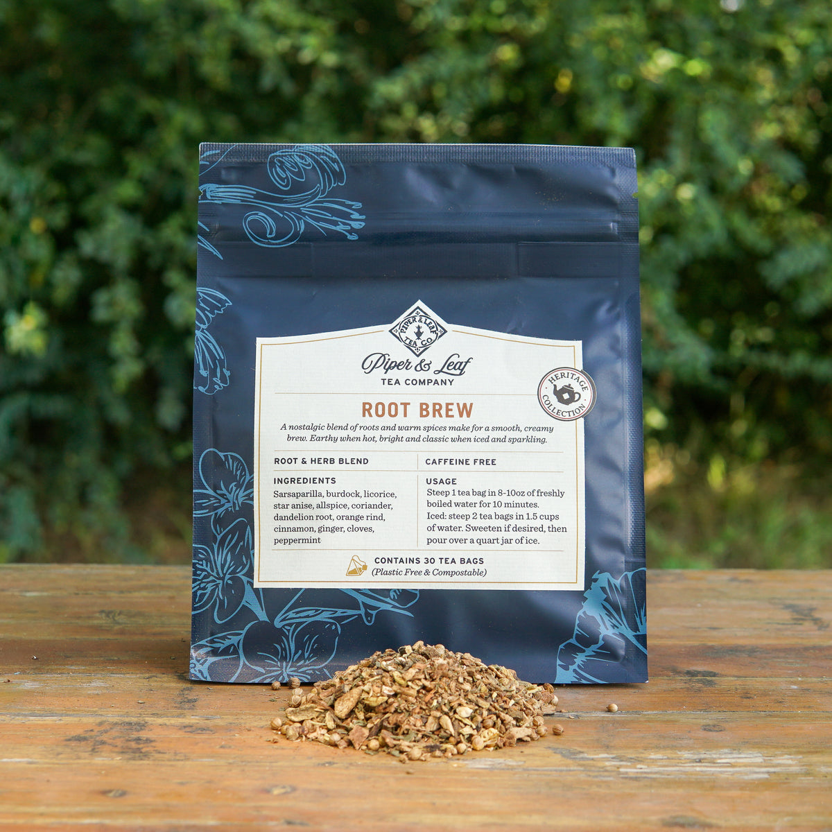 A bag of Root Brew from Piper and Leaf Tea Co. is displayed outdoors on a table, with some loose caffeine-free herbal tea blend scattered in front of the package.