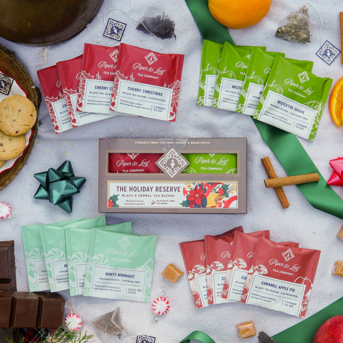 A Holiday Reserve - Box of 16 Tea Bags surrounded by loose rooibos infusion sachets, cookies, chocolate, and seasonal decorations.