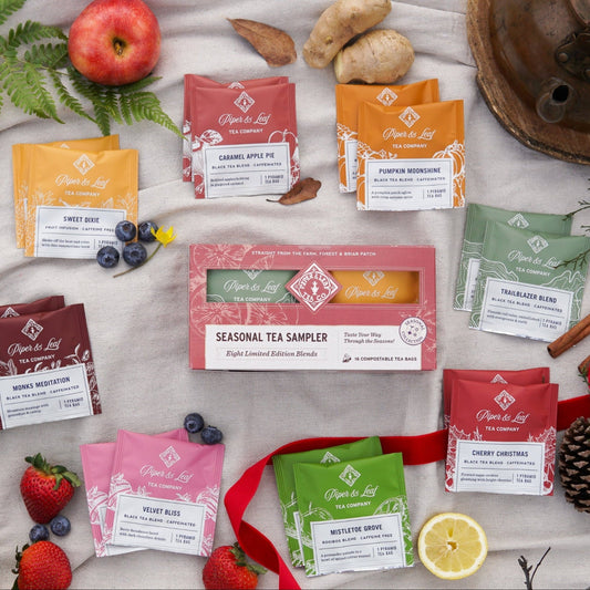 A Piper & Leaf Tea Co. Seasonal Blends Box—featuring 16 tea bags—is displayed on a wooden surface with fruits, spices, pinecones, red ribbon, and a teapot.