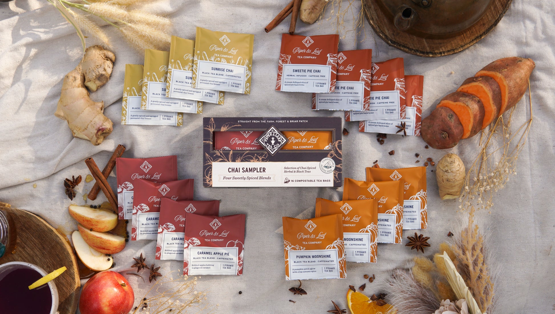 Discover the Piper & Leaf Tea Co. Chai Sampler—Box of 16 Tea Bags, surrounded by fresh ginger, apple, sweet potato, and spices—ideal for tasting cozy autumn blends.