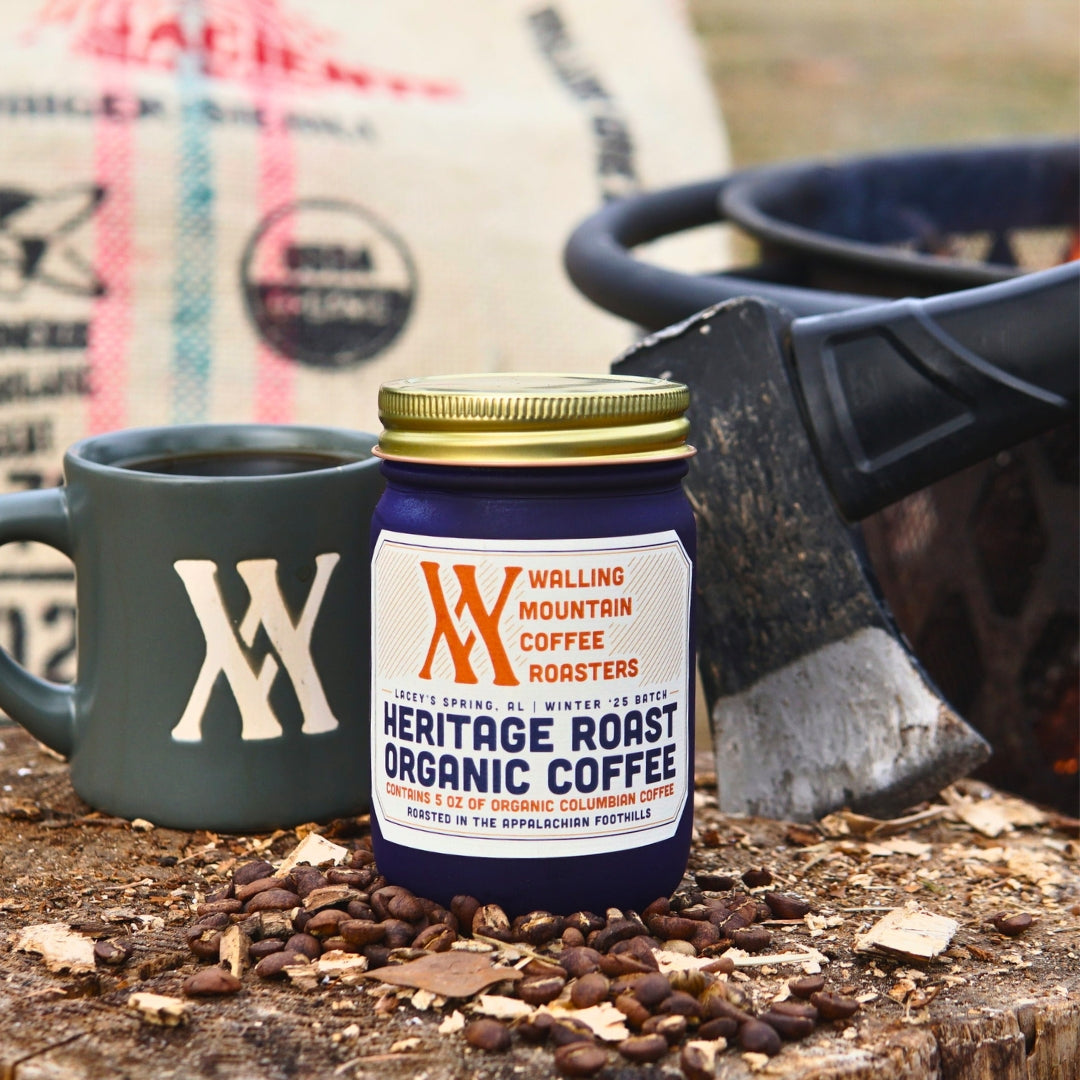 A 5oz Jar of Heritage Roast Coffee from Walling Mtn. Coffee sits beside a gray mug and an axe, scattered with coffee beans, capturing the brand's dedication to quality and tradition.