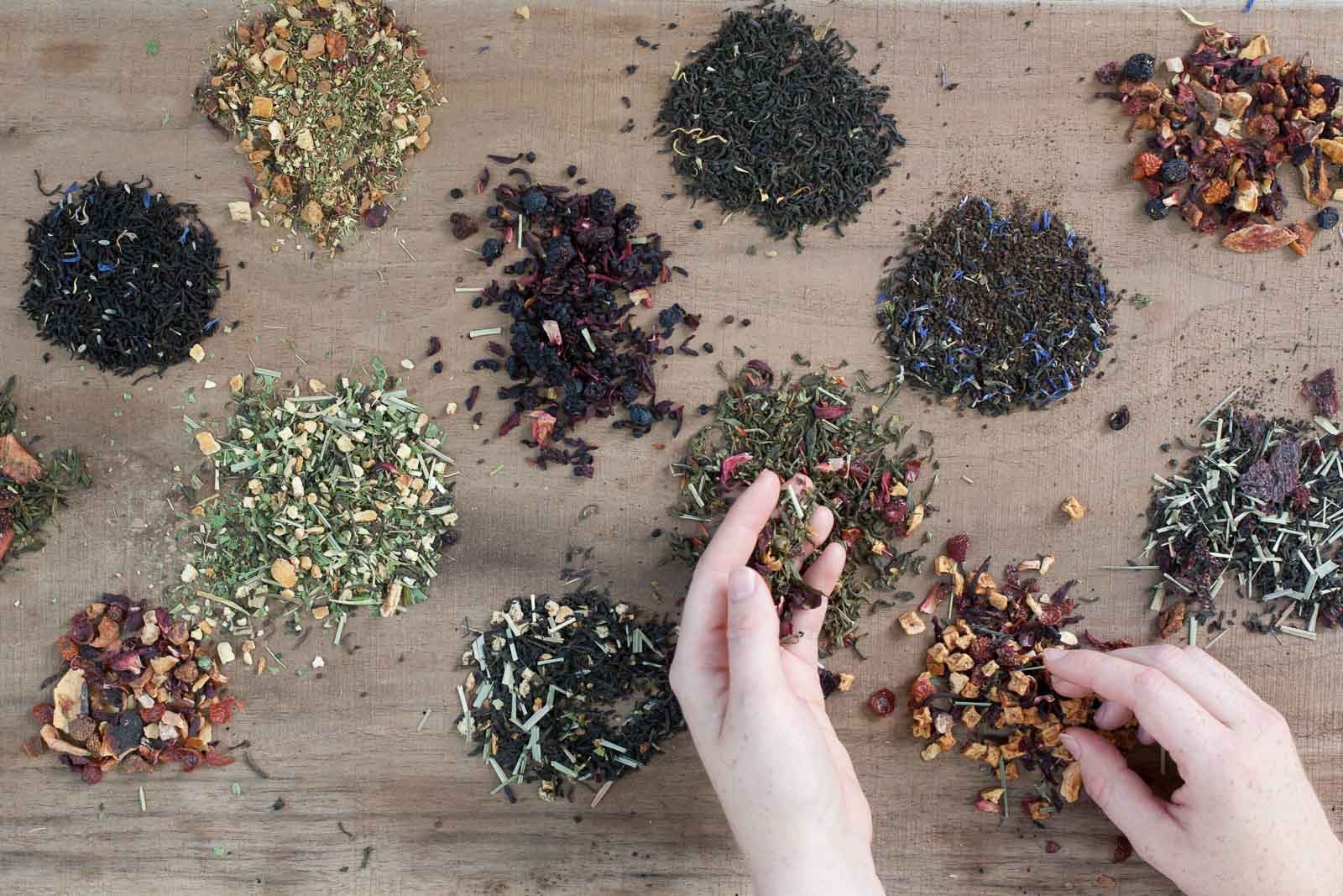 A pair of hands sorting Piper and Leaf Tea Co.'s Mystery 9ct Tea Bags in Muslin, each blend arranged in small piles—a perfect pick for anyone craving an adventurous tea journey.