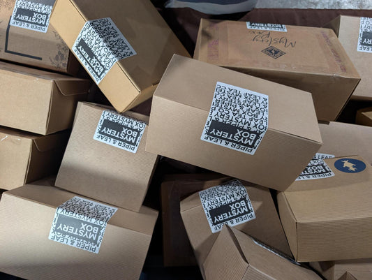 A stack of cardboard boxes, each labeled “Piper and Leaf Tea Co. Mystery Box,” hints at a unique tea gift experience from Piper and Leaf Tea Co.