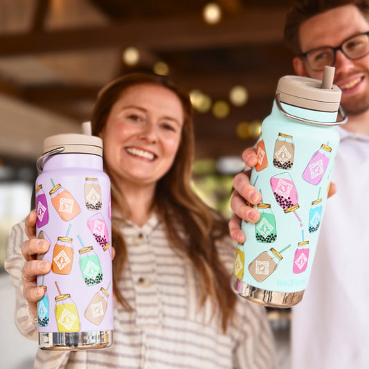 Two people hold limited edition 32oz Klean Kanteens by Piper & Leaf Tea Co., colorful water bottles with straw lids and jar illustrations. Made from BPA-free stainless steel, they are double-walled vacuum insulated to keep drinks at the perfect temperature.