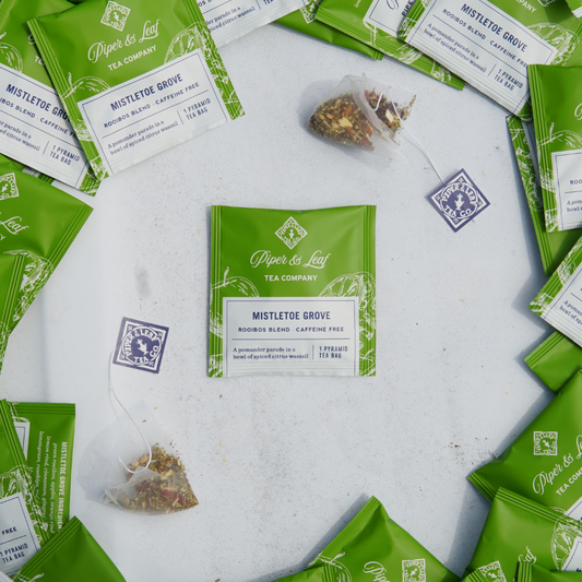 Tea bags from Piper & Leaf Tea Co.'s "Mistletoe Grove Case of Individually Wrapped Tea Bags- 50ct" are elegantly arranged in a circle with two packets on a light surface, ideal for an elegant tea party.