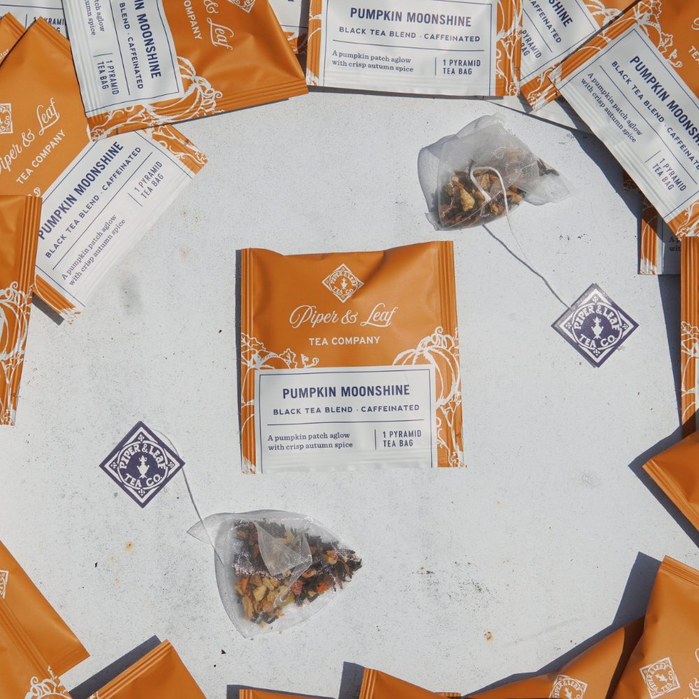 Several orange packages of "Pumpkin Moonshine Case of Individually Wrapped Tea Bags- 50ct" by Piper & Leaf Tea Co. are arranged around tea sachets on a flat surface, perfect for stocking in the break room.