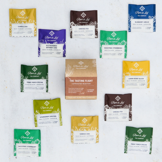 A colorful assortment of Piper & Leaf Tea Co.'s caffeinated tea blends encircles a central Caffeinated Tasting Flight - Box of 12 Tea Bags, all displayed against a clean white background.