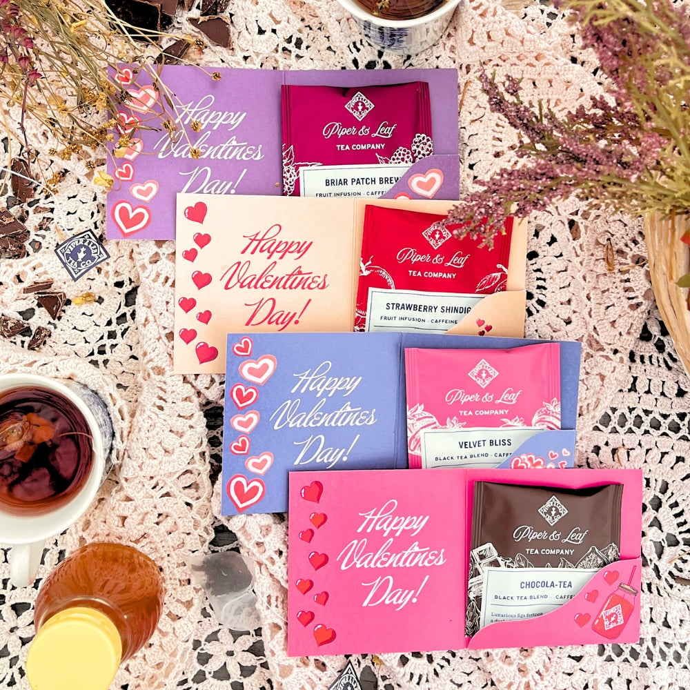 A Valentine-themed display showcases Piper & Leaf Tea Co.'s Tea Valentines assortment on a lace tablecloth, surrounded by flowers and drinks.