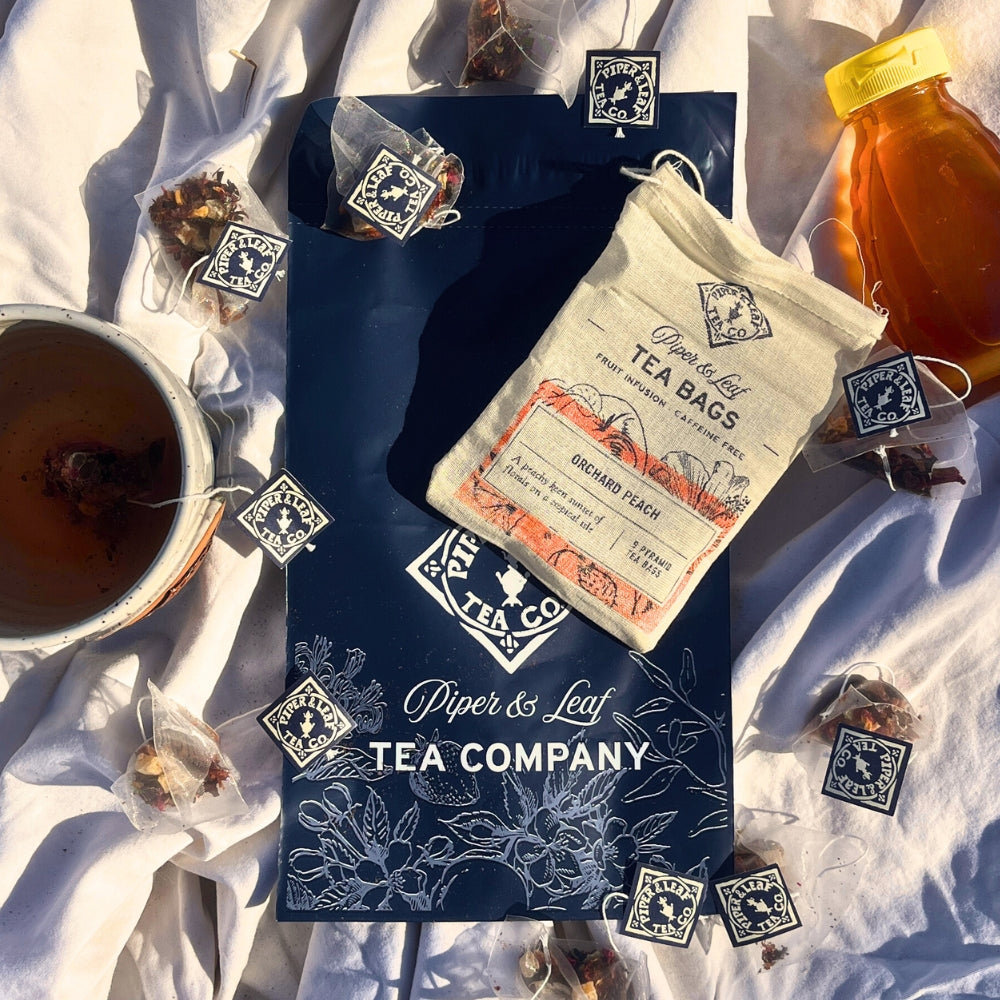 Explore Piper & Leaf Tea Co.'s Tea Subscription in our ad, featuring a Tea of the Month package with a mug, aromatic tea bags, and a jar of honey on a white cloth.