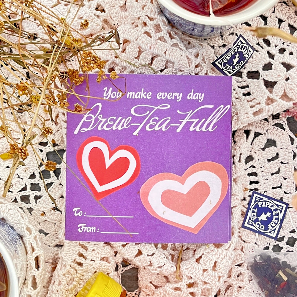 The Tea Valentines card by Piper & Leaf Tea Co. features a purple design with white text, "You make every day Brew-Tea-Full," two heart shapes, and "To:" and "From:" spaces. Surrounded by dried flowers, tea cups, and berry best blends—ideal for a Valentine's Day tea surprise.