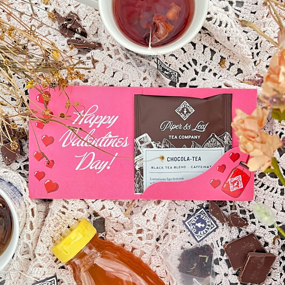 The "Tea Valentines" card by Piper & Leaf Tea Co. showcases a Chocola-tea packet, surrounded by Valentine's tea cups, a honey bottle, chocolates, and dried flowers on a lace cloth.