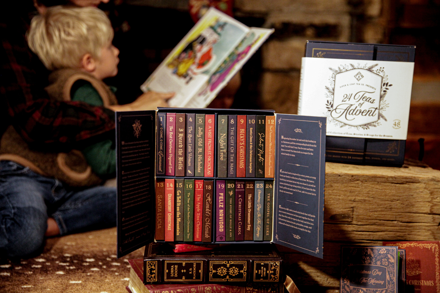 Close-up of the 24 Teas of Advent—Piper and Leaf Advent Calendar 2024 by Piper & Leaf Tea Co. featuring 24 numbered tea boxes. A child reads a book in the blurred background.